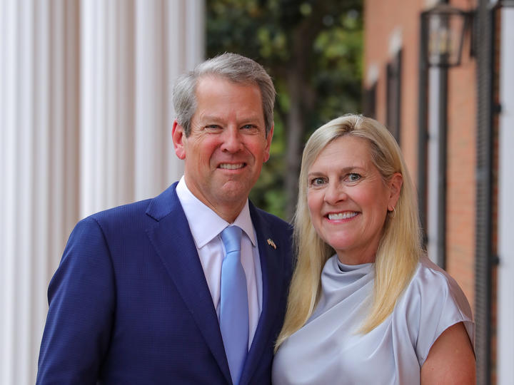 Governor Brian Kemp and his wife First Lady Marty Kemp stand smiling in front of a large building